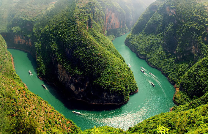 Green river winding through lush mountains with boats cruising, showcasing natural beauty and top reasons to visit China.