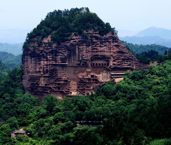 Ancient cliffside temple carved into rock surrounded by lush greenery, showcasing a unique attraction to visit in China.