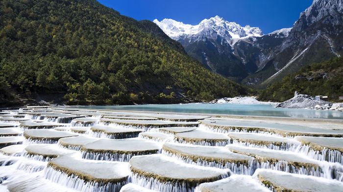 Terraced waterfalls in a mountainous landscape showcasing natural beauty in China for travel and tourism.