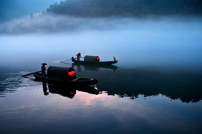 Traditional Chinese boats with red lanterns floating on misty river at dawn, showcasing serene travel moments in China.