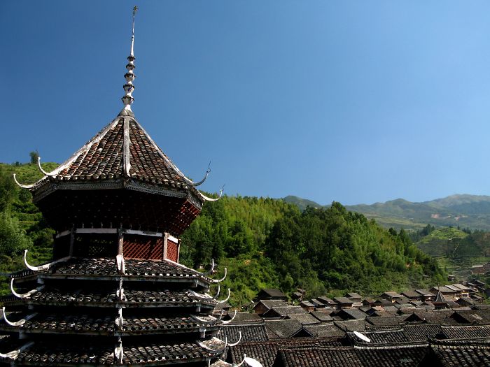 Ancient traditional Chinese pagoda overlooking a village with lush green hills under a clear blue sky.