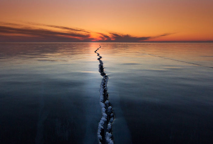 Sunset over calm icy water with a long crack stretching toward the horizon in National Geographic top photos.