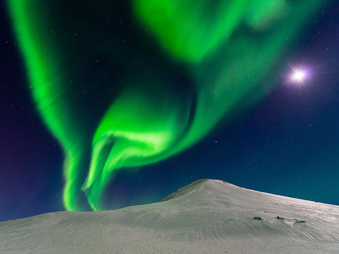 Northern lights display vibrant green colors over a snowy mountain under a starry night sky, featured in top photos.
