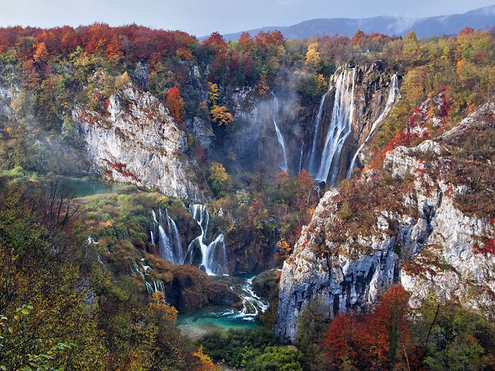 Autumn waterfalls cascading through rocky cliffs surrounded by colorful trees in National Geographic top photos 2015.