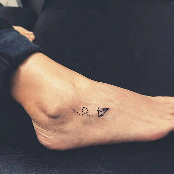 Black small paper plane flying tattoo on foot