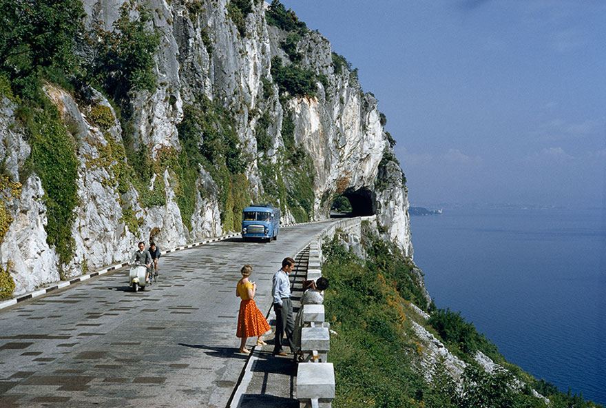 Motorists Pass People On A Scenic Road Atop A Cliff Overlooking A Bay Near Trieste, Italy, 1956