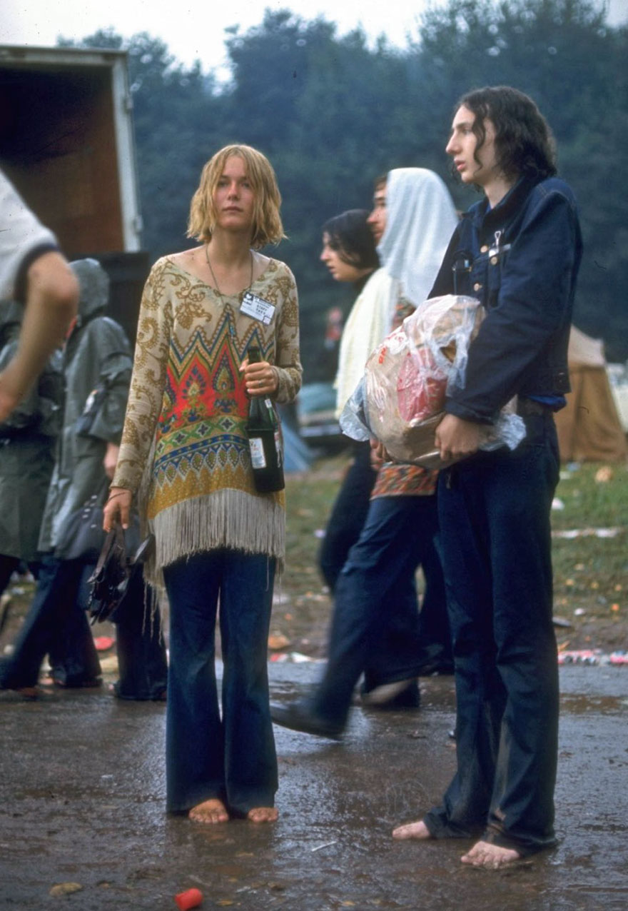 Hippie Couple Standing Barefoot On A Road Holding A Bundle & Wine Bottle At Woodstock