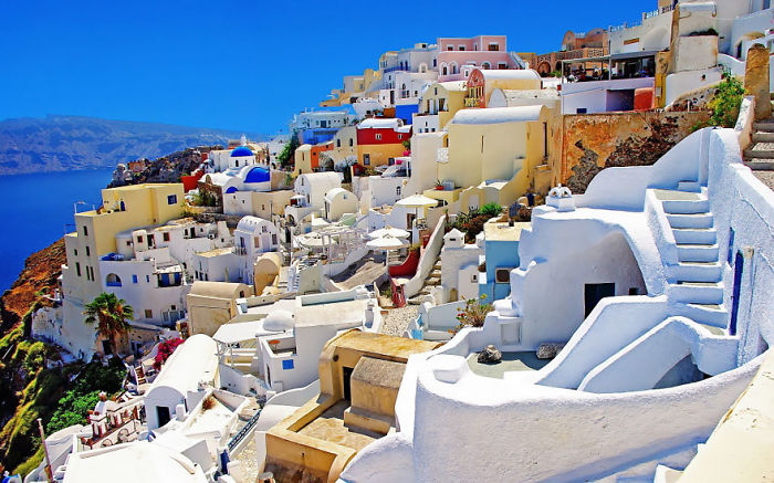 Colorful fairy tale village with whitewashed buildings on a hillside, under a bright blue sky.