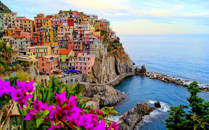 Colorful fairy tale village by the sea, with vibrant flowers and dramatic cliffs.