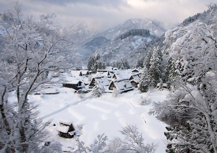 Snow-covered fairy tale village nestled in a mountainous landscape with traditional houses and frosted trees.