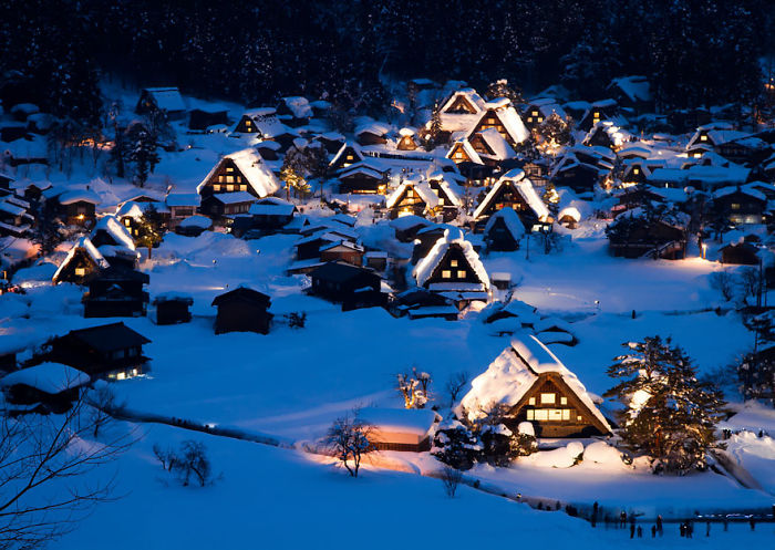 Fairy tale village with snow-covered, illuminated houses at dusk, creating a magical winter scene.