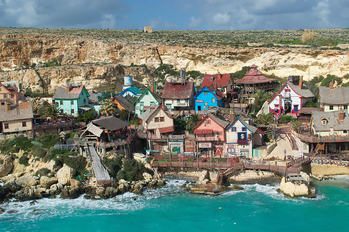 Colorful fairy tale village by the sea, with vibrant houses and rocky cliffs in the background.