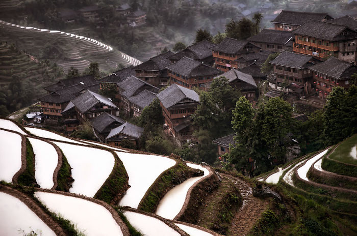 Fairy tale village with traditional houses surrounded by lush greenery and terraced fields.