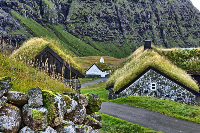 Fairy tale village with grass-roofed houses nestled in a green mountain landscape.