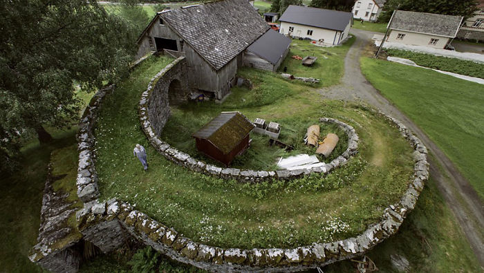 Fairy tale village scene with spiral stone wall and rustic barn surrounded by lush greenery.
