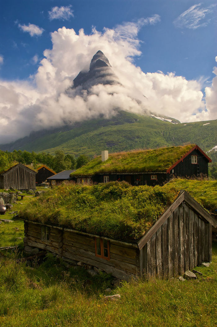 Fairy tale village with grass-roofed cottages beneath a misty mountain peak.
