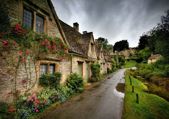 Fairy tale village with charming stone cottages and lush greenery under a cloudy sky.