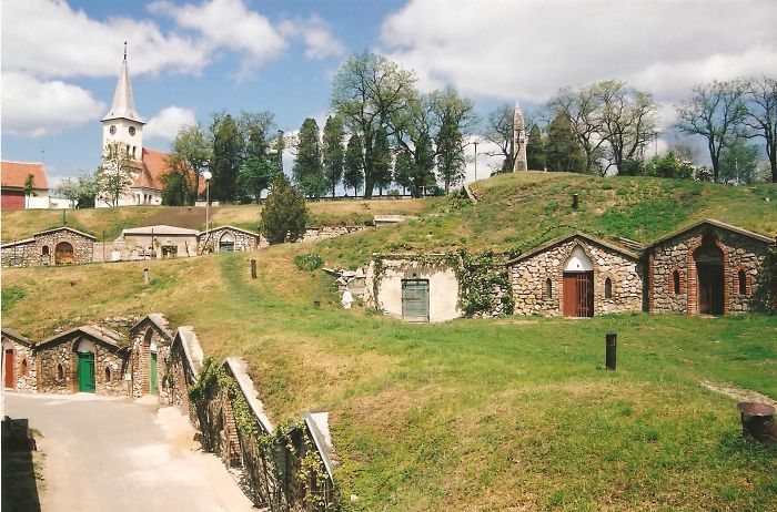 Fairy tale village with quaint stone houses and a church, surrounded by lush greenery and trees.