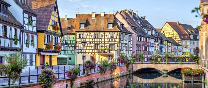 Fairy tale village with colorful half-timbered houses along a canal, adorned with flowers and a picturesque bridge.