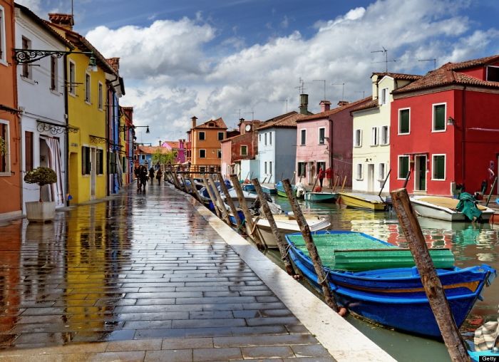 Colorful fairy tale village with boats lined along the canal and vibrant houses reflecting on a wet cobblestone street.