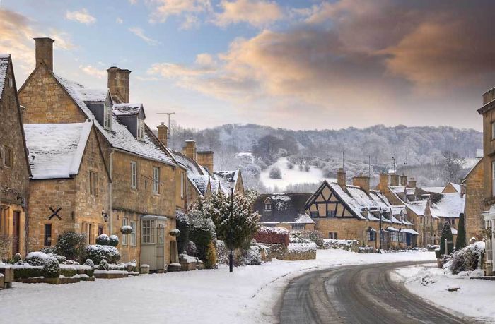 Snow-covered fairy tale village scene with charming stone cottages and a winding road.