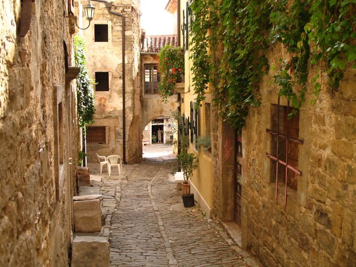Cobblestone street in a fairy tale village with rustic stone buildings and lush greenery.