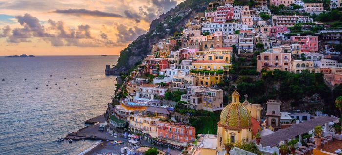 Colorful buildings on a cliffside village by the sea at sunset, showcasing a fairy tale atmosphere.