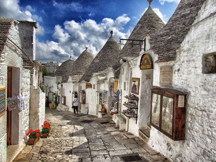 Quaint stone houses with conical roofs in a fairy tale village under a vibrant blue sky.
