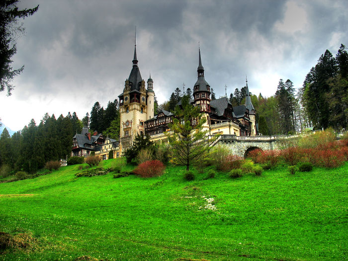 Fairy tale village castle surrounded by lush greenery and dramatic skies.