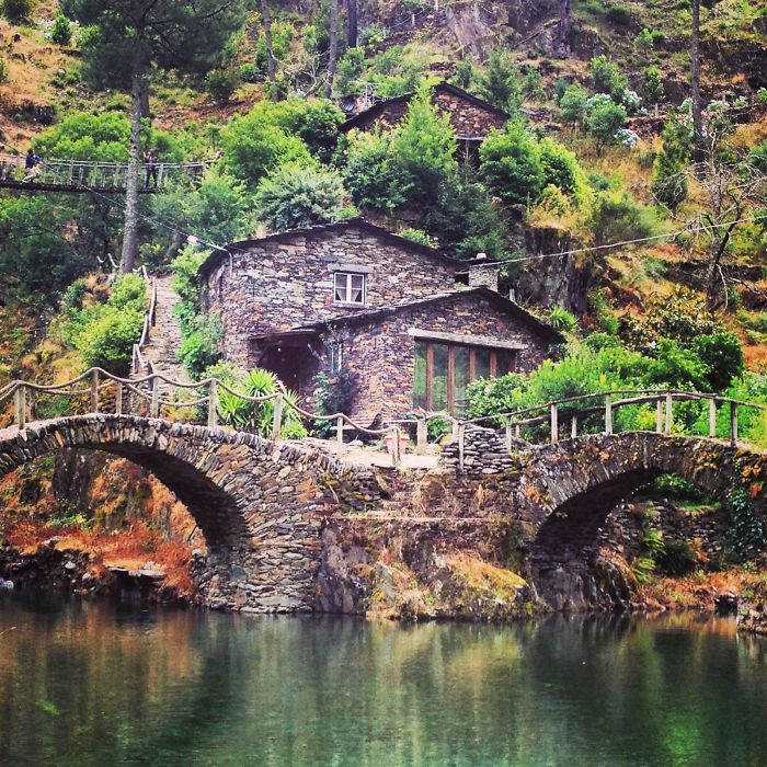 Stone bridge leading to a charming fairy tale village house nestled in lush greenery.