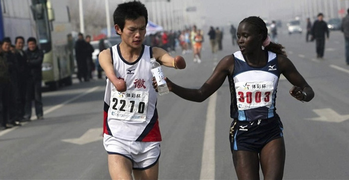 Woman Handing A Bottle Of Water To A Fellow Runner Without Hands