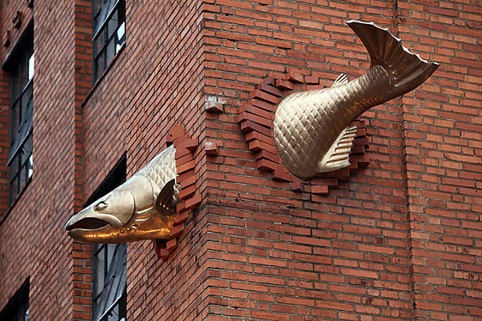 Gold fish sculpture emerging from brick wall corner on building facade, an amazing sculpture in the world.