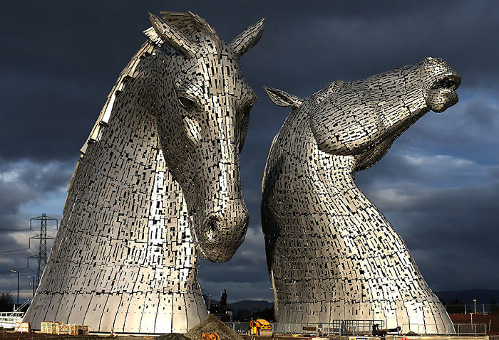 Two large metal horse head sculptures standing outdoors under a dark cloudy sky, showcasing amazing sculptures.