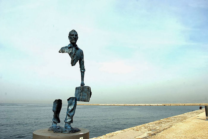 Abstract sculpture of a man with floating torso and legs holding a briefcase, viewed against a calm sea background.