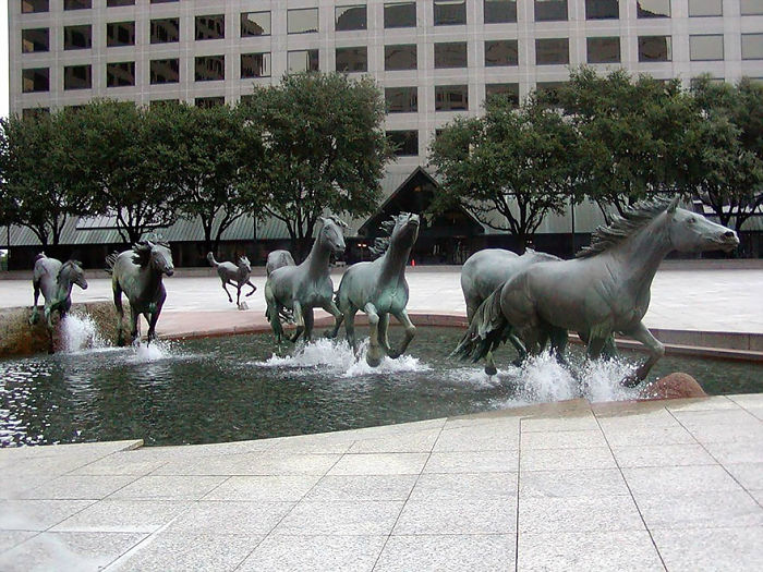 Bronze horse sculptures running through water in an urban plaza, showcasing one of the most amazing sculptures in the world.