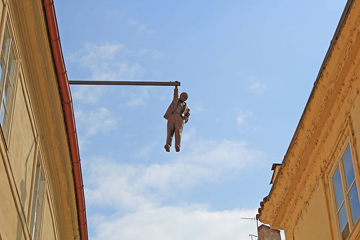 Bronze sculpture of a man hanging from a pole between two buildings against a clear blue sky, an amazing sculpture in the world.