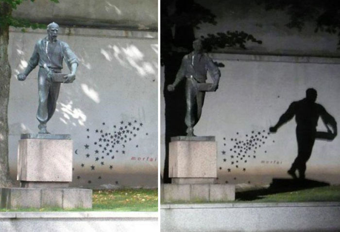 Metal sculpture of a man scattering stars, casting a shadow that creatively interacts with the wall behind at night.