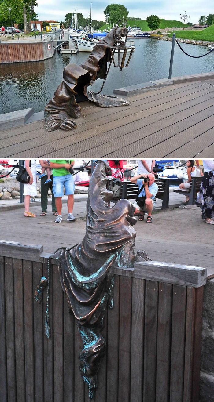 Two views of an amazing sculpture of a cloaked figure climbing over a wooden dock near a marina with boats and people.