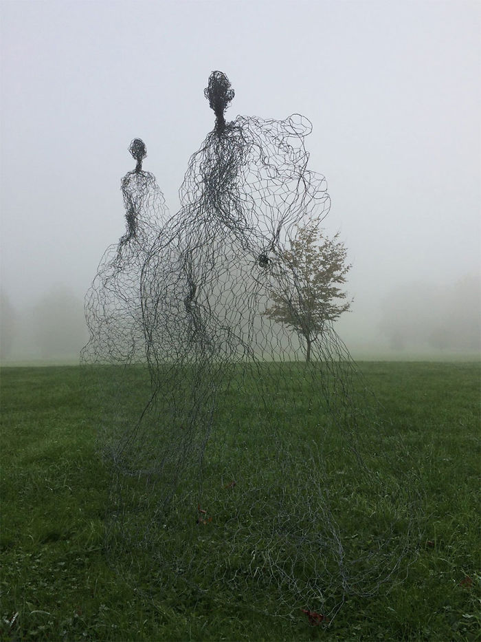Wire mesh sculptures of two human figures standing on grass in a foggy outdoor setting showcasing amazing sculptures in the world.
