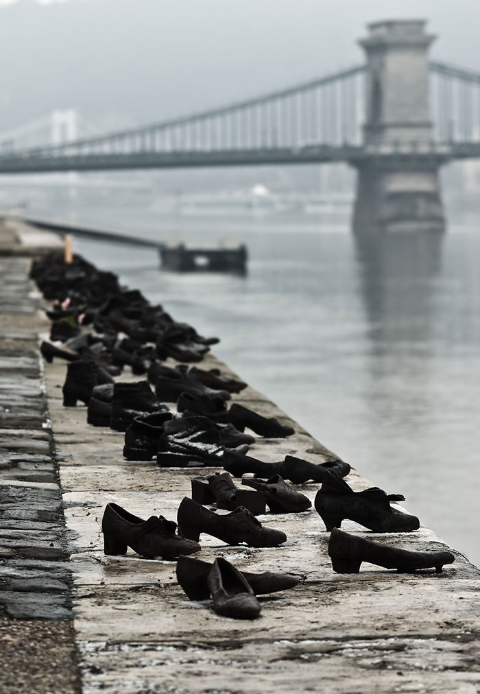 Shoes sculpture installation along riverbank near a bridge, representing one of the most amazing sculptures in the world.