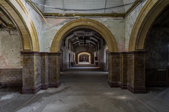 Abandoned Britain hallway with ornate arches and tiled walls showing decay in an old abandoned place in the UK.