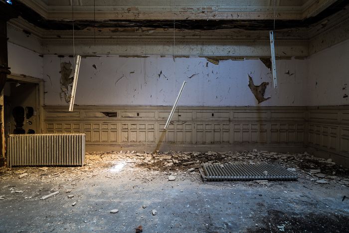 Abandoned Britain interior of a decayed room with peeling walls, broken floor, and old radiators in a deserted UK building.