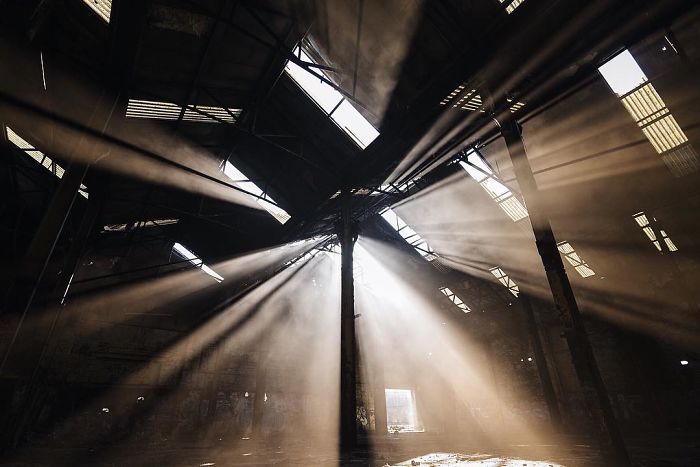 Sunlight beams streaming through broken windows inside an abandoned Britain industrial building with dust in the air.