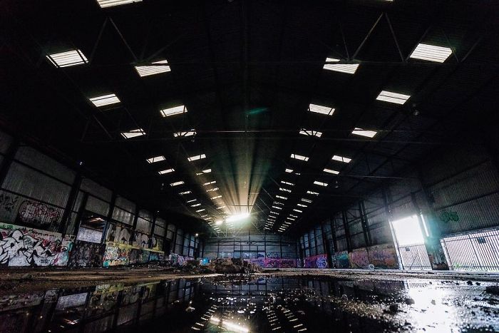 Abandoned Britain industrial warehouse with graffiti-covered walls and sunlight streaming through broken roof windows.