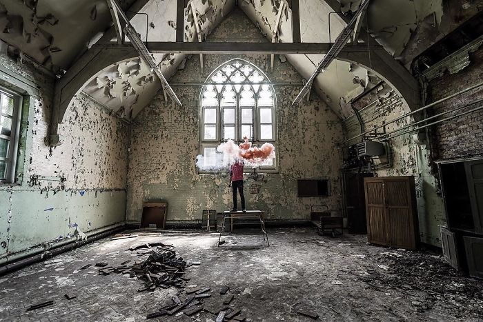 Photographer standing on a table inside an abandoned building in the UK, capturing images of decaying interiors.