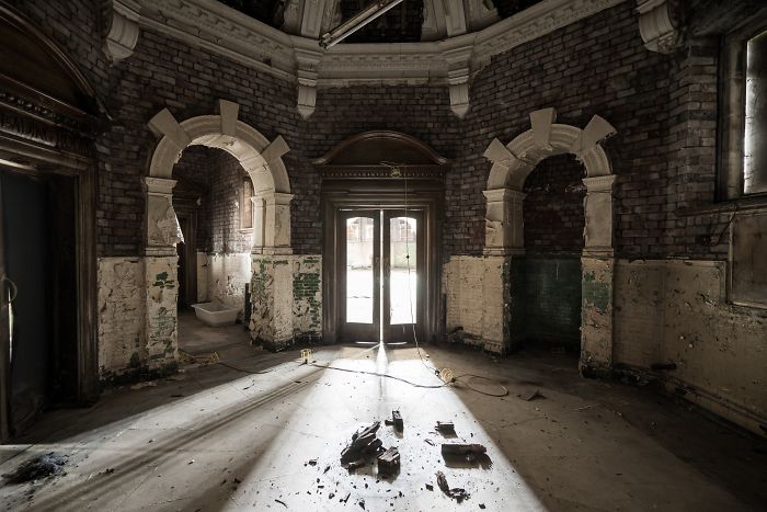Interior of an abandoned building in Britain with damaged brick walls and sunlight streaming through shattered windows.