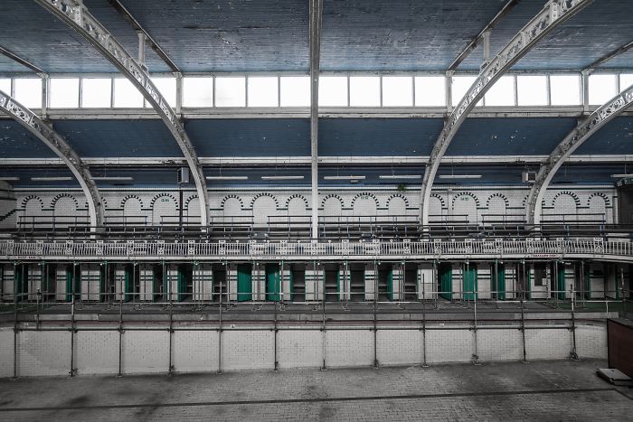Abandoned Britain indoor view of an empty historic swimming pool with metal arches and large windows above.