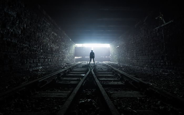 Person standing on abandoned railway tracks inside a dark tunnel, capturing the essence of abandoned Britain places.