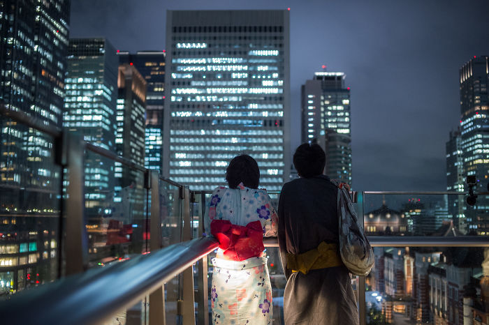 Two people in traditional clothing overlooking illuminated skyscrapers in a Japan street photography night scene.
