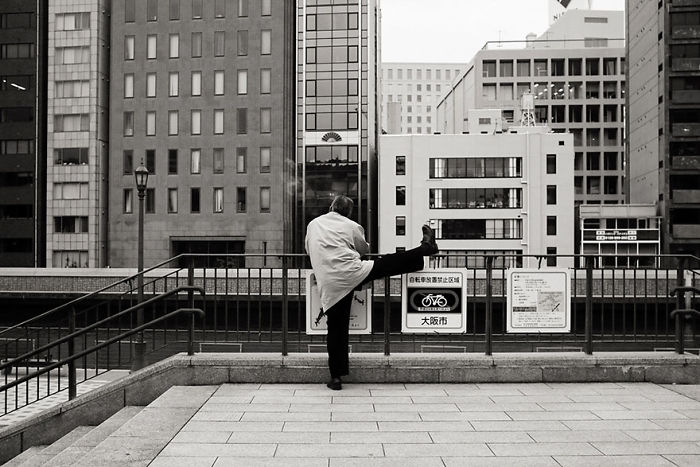 Man stretching leg on railing in urban setting, showcasing Japan street photography capturing the rarely seen side of the city.
